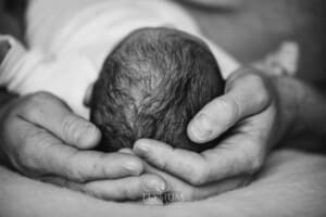 A fathers hands hold his newborn baby girl