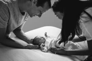 Parents lean over their newborn baby girl as she looks up at them
