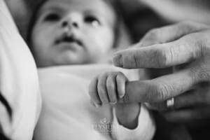 A tiny newborn baby's hand grips her fathers finger