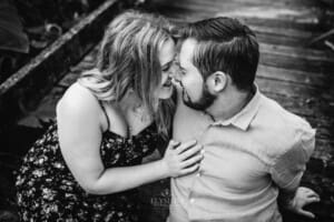 A couple sit on a boardwalk with their foreheads pressed together