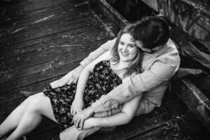 A man hugs his fiancée as they sit on a boardwalk
