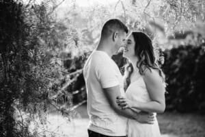 An engage couple hug standing under a tree at sunset
