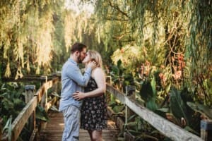 A couple stand and share a kiss on a boardwalk at sunrise