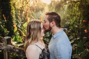 A man kisses his fiancée on the forehead as they stand on a boardwalk