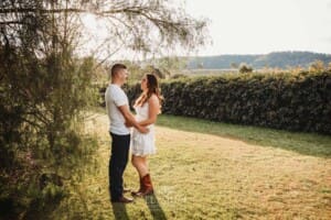 An engage couple hug standing under a tree at sunset