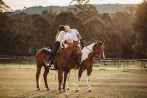 An engaged kiss on horseback in a field at sunset