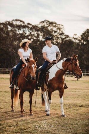 An engaged couple stand with their horses at sunset