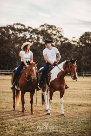 An engaged couple stand with their horses at sunset