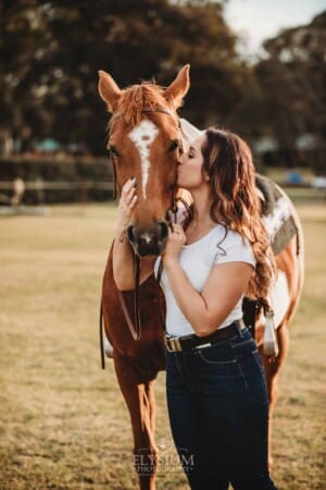 A woman kisses her horse in a field at sunset