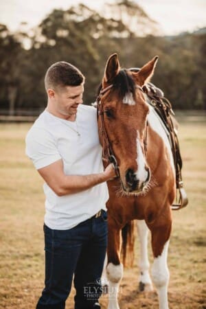 A man stands with his horse in a field at sunset