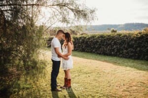 An engage couple hug standing under a tree at sunset