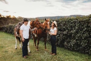 An engaged couple stand with their horses at sunset