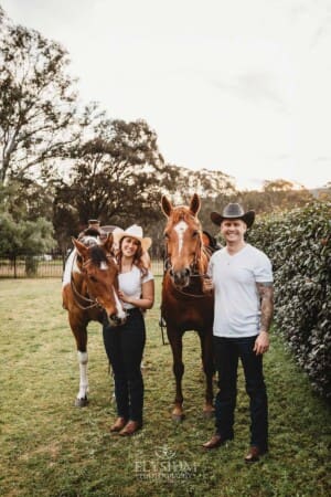 An engaged couple stand with their horses at sunset