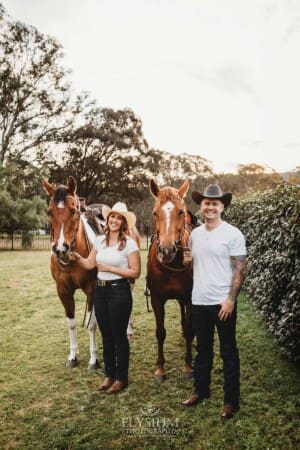 An engaged couple stand with their horses at sunset