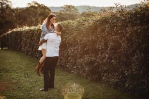 A man picks up and spins his fiancée in a field at sunset