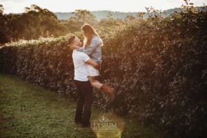 A man picks up and spins his fiancée in a field at sunset