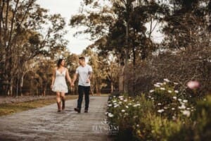 An engage couple walk along a path holding hands at sunset