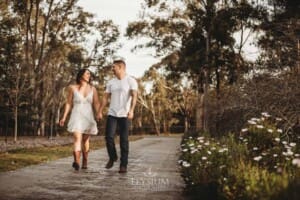 An engage couple walk along a path holding hands at sunset