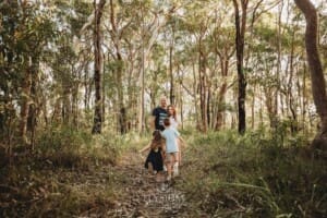 Children run towards their parents standing on a bush track at sunset