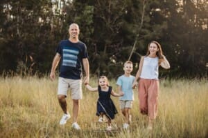 Parents walk along with their children through a grassy field at sunset