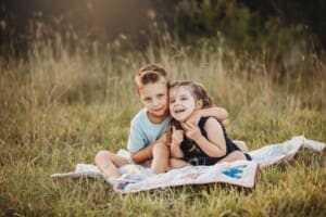 Children sit on a bright coloured rug in a grassy field at sunset