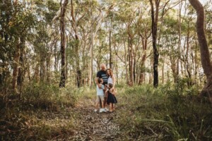 Children hug their parents standing on a bush track at sunset