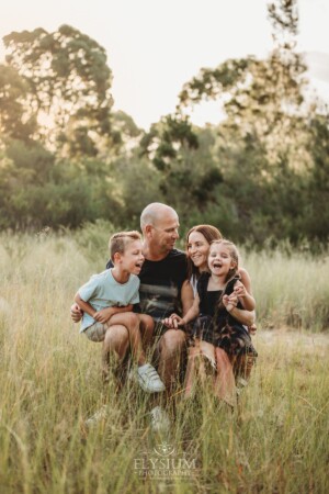 Parents sit laughing with their children in a grassy field at sunset