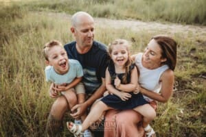 Parents sit laughing with their children in a grassy field at sunset