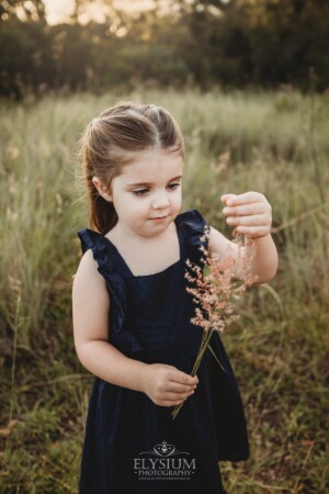 A little girl picking wildflowers in a grassy field at sunset