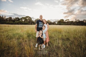 Parents hug their children standing in a grassy field at sunset
