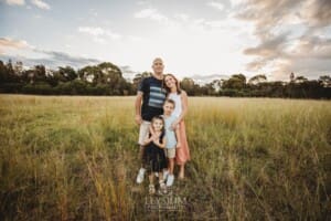 Parents hug their children standing in a grassy field at sunset