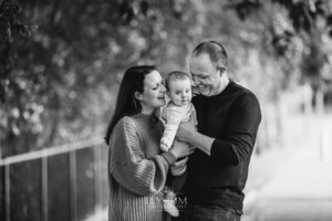 Baby photography - A family hug their baby girl between them standing under a tree