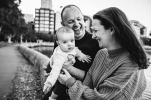 Baby photography - A family cuddle their baby girl in their lap as they sit beside the water