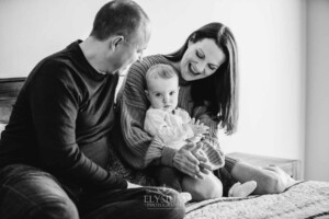 Baby photography - parents sit on a bed with their little girl in their lap