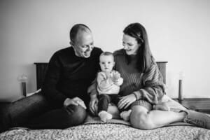 Baby photography - parents sit on a bed with their little girl in their lap