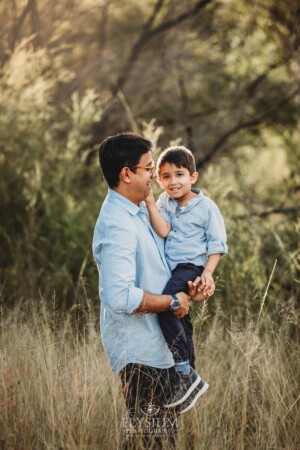 Family Session - A father cuddles his little boy as they stand in long grass