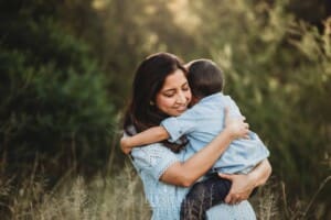 Family Session - A mother cuddles her son as they stand in long grass at sunset