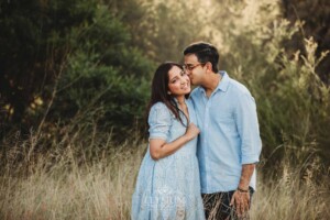Family Session - A man kisses his wife on the cheek as they stand in long grass