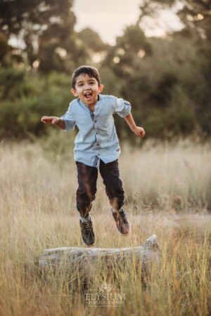 Family Session - a little boy leaps off a log into long grass at sunset