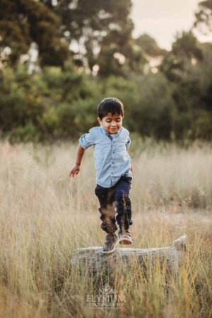 Family Session - a little boy jumps off a log into long grass at sunset