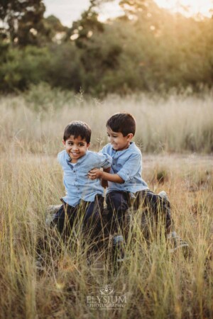 Family Session - brothers sit on a log tickling each other at sunset