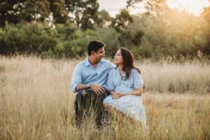 Family Session - parents sit cuddled together on a log surrounded by long grass