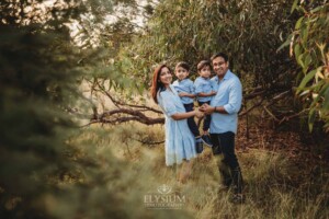 Family Session - parents hug their little boys as they stand amongst leafy trees