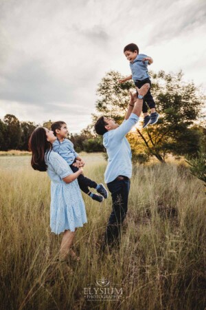 Family Session - a father hoists his son into the air in a grassy field at sunset