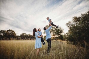 Family Session - a father hoists his son into the air in a grassy field at sunset