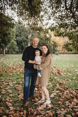 Baby photography - A family cuddle their little girl standing in a park under a tree