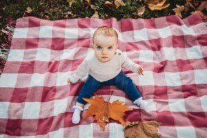 Baby photography - a little girl sits on a checkered blanket with an orange leaf