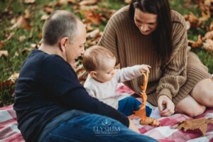 Baby photography - a little girl plays with an autumn leaf sitting on a blanket with her parents