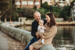 Baby photography - parents cuddle their baby girl as they sit beside the water