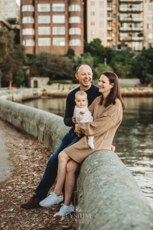 Baby photography - parents cuddle their baby girl as they sit beside the water